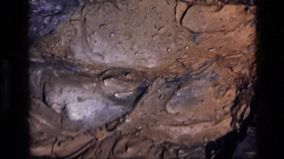 1972 Idaho 8mm frame emphasizing a tight section of brown pigmented rock with pits, shadows, and smooth glossy contours.