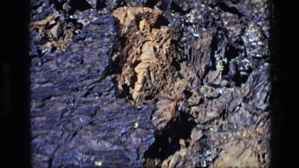 1972 Idaho 8mm frame showing darker jagged rock with tan mineral material, layered texture, and strong directional light.