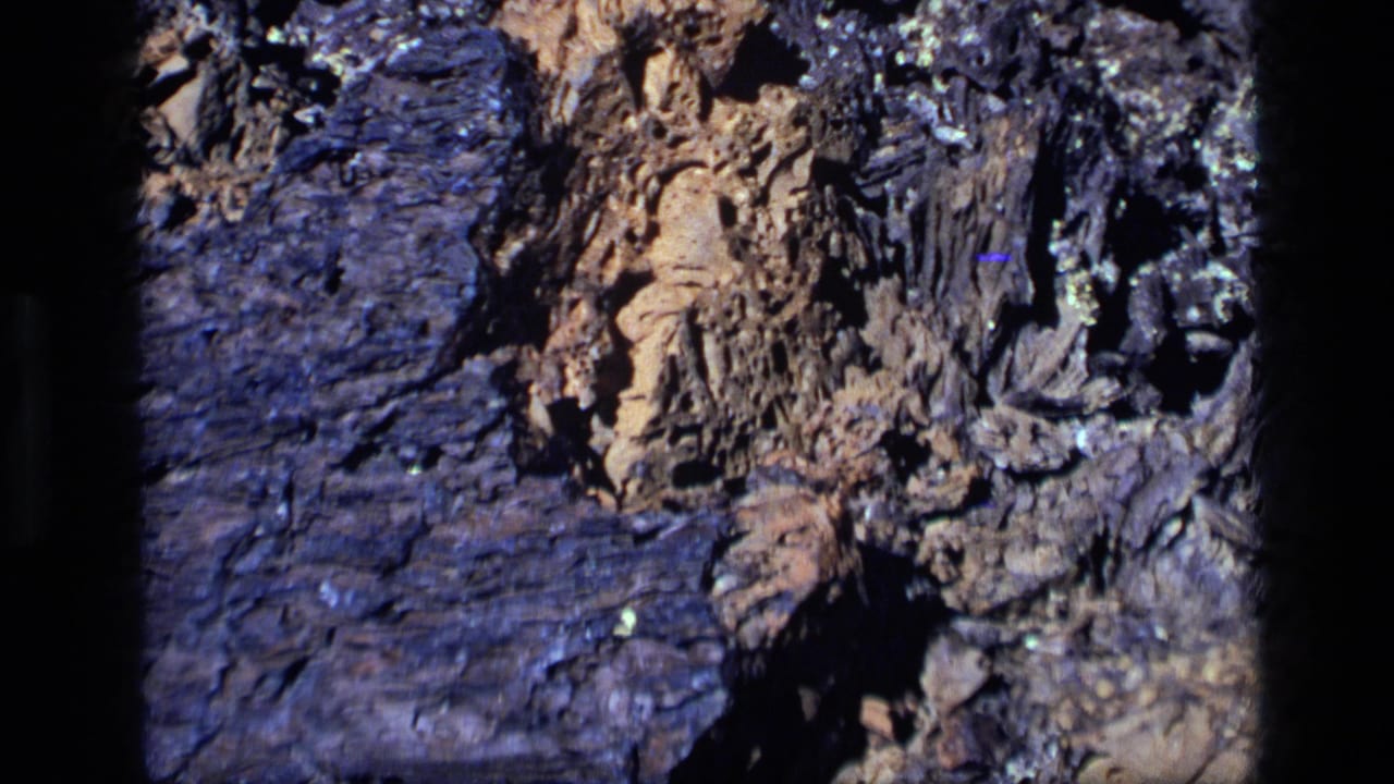 1972 Idaho 8mm frame showing a close-up of weathered rock layers with tan stone, dark bluish areas, and deep crevices.