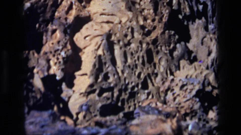 1972 Idaho 8mm frame showing eroded tan rock forms with small cavities, dark shadow areas, and bluish stone at the side.