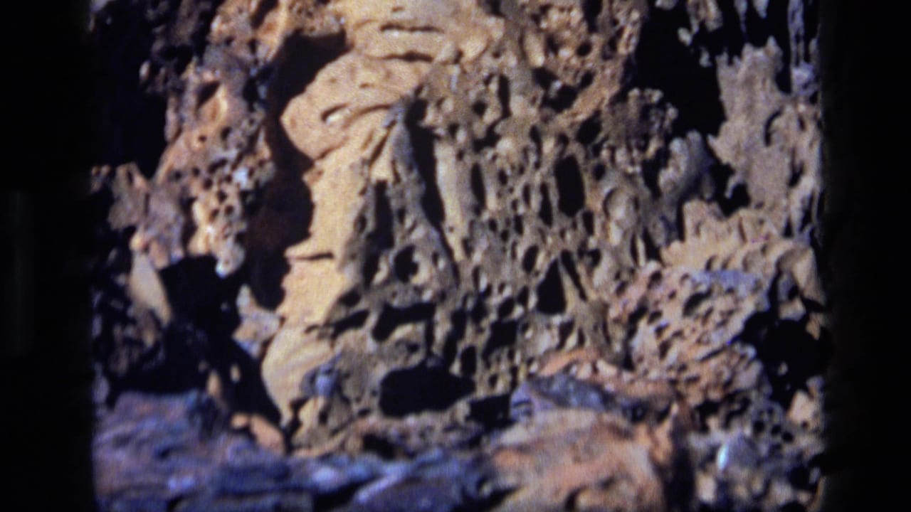 1972 Idaho 8mm frame showing textured lava rock in close-up, with rough holes and dark shadows across the surface.