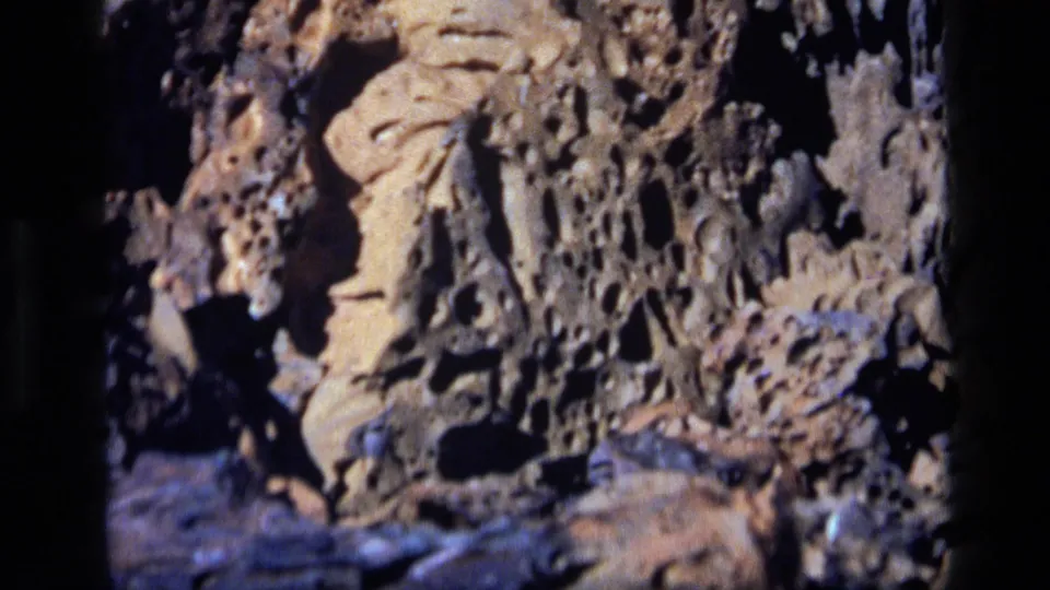 1972 Idaho 8mm frame showing textured lava rock in close-up, with rough holes and dark shadows across the surface.