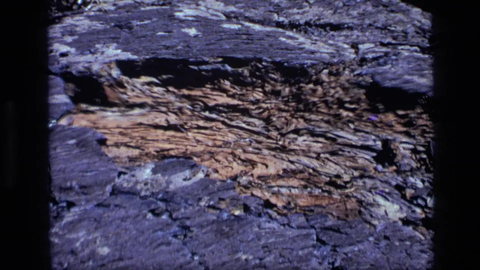 1972 Idaho 8mm frame with a wider view of dark, rough stone surrounding an exposed orange-brown weathered rock layer.