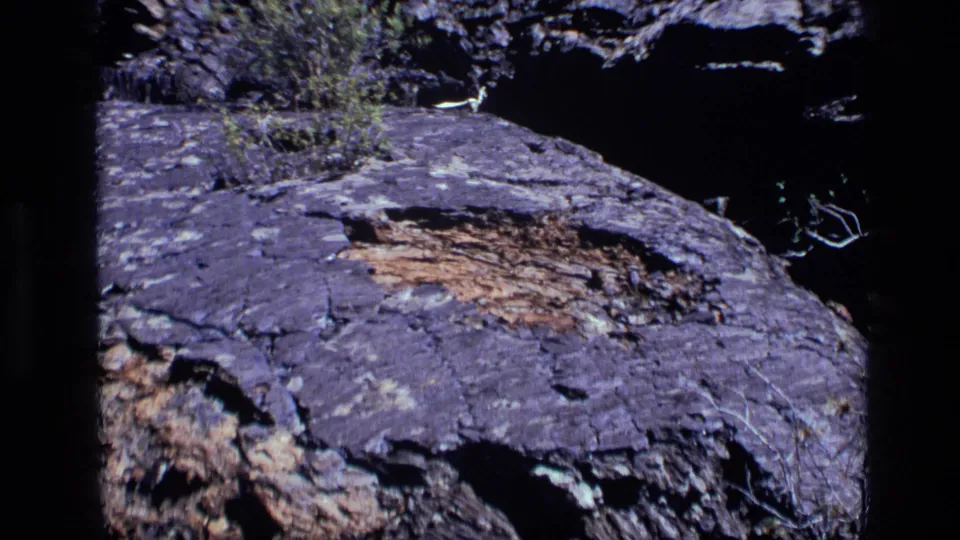 1972 Idaho 8mm frame with purple-gray layered rock, visible cracks, and a dark shadowed background around the stone.