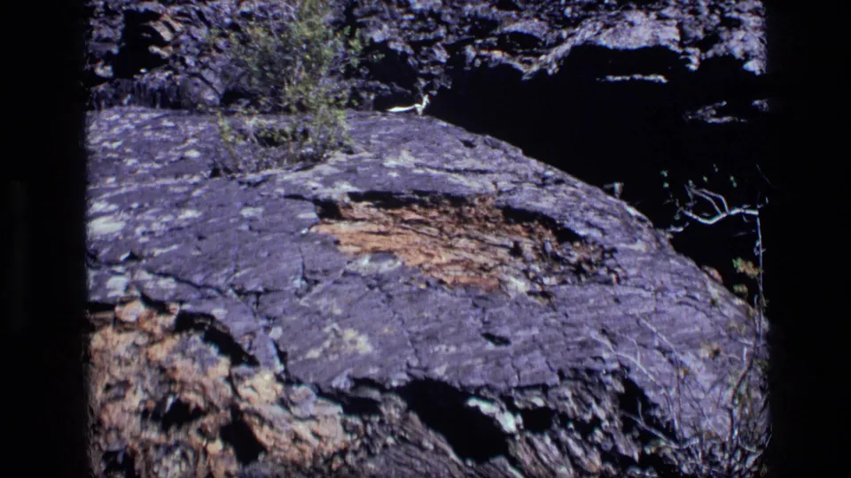 1972 Idaho 8mm frame showing a rugged layered rock face with cracks, brown patches, and soft home-movie color shift.