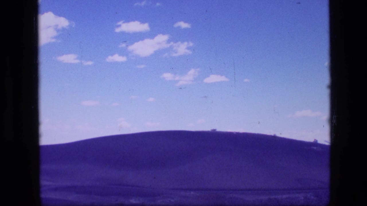 1972 Idaho 8mm frame showing a distant rounded hill, open blue sky, small clouds, and visible film gate edges.