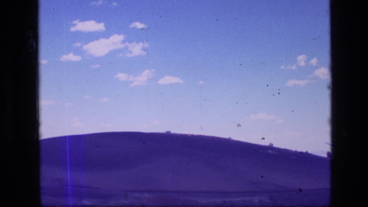 Low hill and wide clouded sky seen through dark vertical film borders.