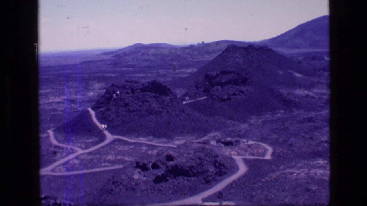 Wide view of dry hills, rocky cones, and pale dirt roads under a hazy sky.