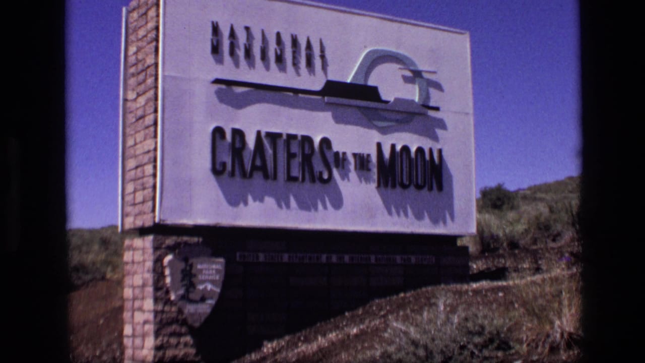 Craters of the Moon sign on a brick base beside scrubby terrain.
