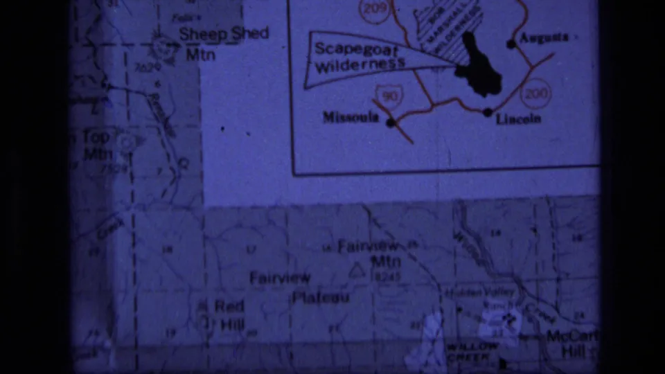1973 8mm frame showing a projected Montana map with Scapegoat Wilderness inset and surrounding mountain labels.