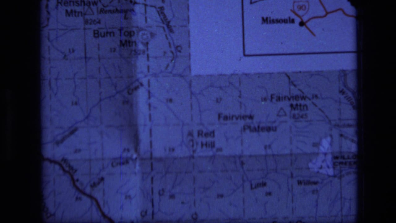 1973 8mm frame of a projected Montana map section showing Fairview Mountain, Red Hill, roads, and grid markings within dark film-gate edges.
