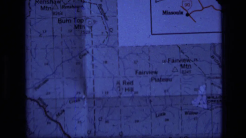 1973 8mm frame of a projected Montana map section showing Fairview Mountain, Red Hill, roads, and grid markings within dark film-gate edges.