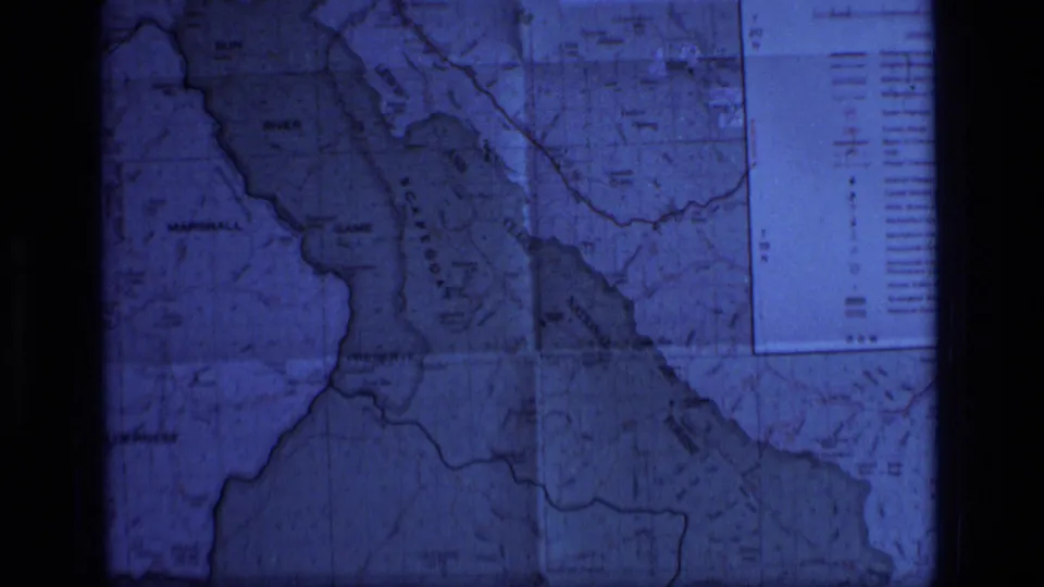 Blue-tinted 8mm frame of the Montana wilderness map showing Scapegoat Wilderness, a lake area, boundary lines, and a printed legend panel.