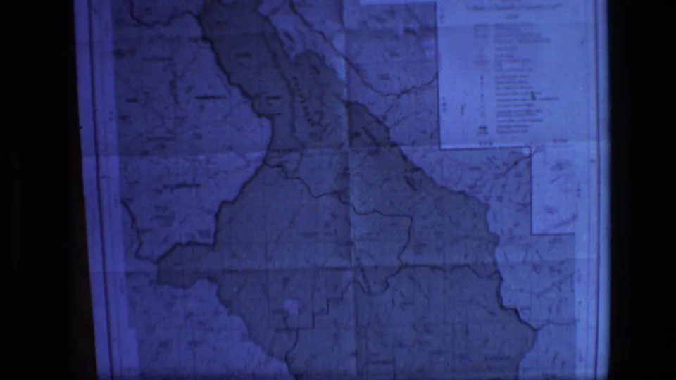 1973 home-movie frame showing the projected Scapegoat Wilderness map, with a blue cast, soft focus, boundary lines, and legend area.