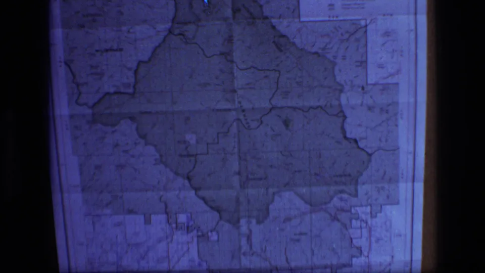 Archival 8mm frame of the Scapegoat Wilderness map projection, softened by grain, blue exposure, and projection distortion.