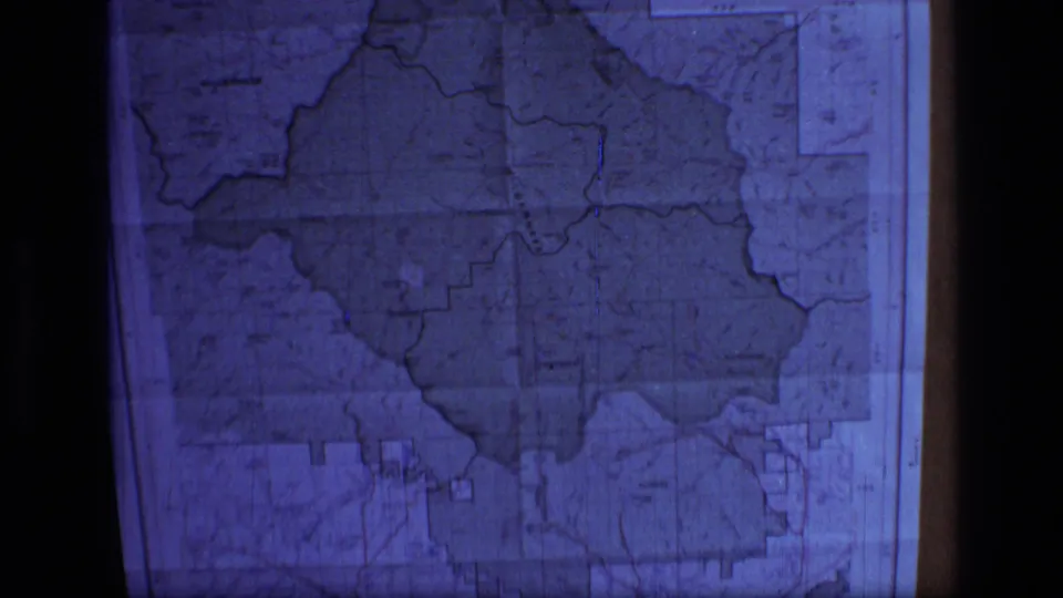 1973 8mm frame showing a blue-tinted close-up of a framed Scapegoat Wilderness area topographic map in Montana.