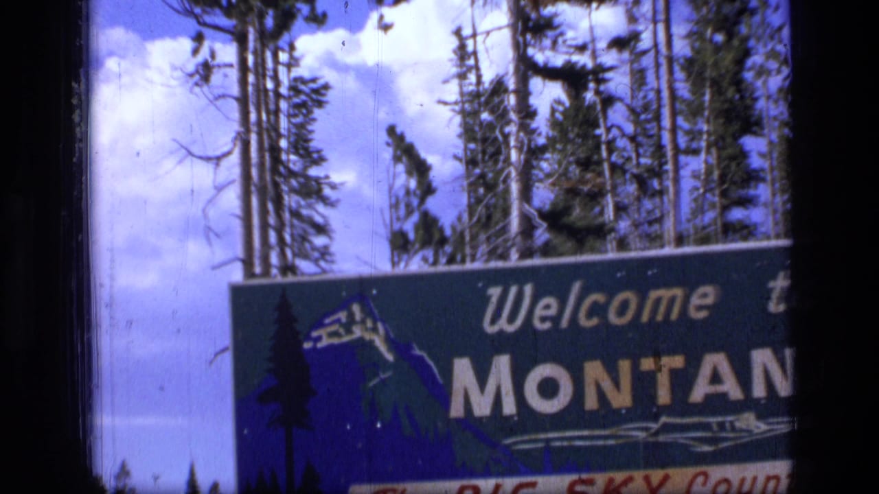 Montana welcome sign beside tall trees under a blue sky.