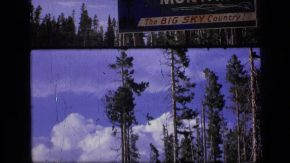 1973 Montana travel footage frame showing tall pines and white clouds within an 8mm contact-sheet border.