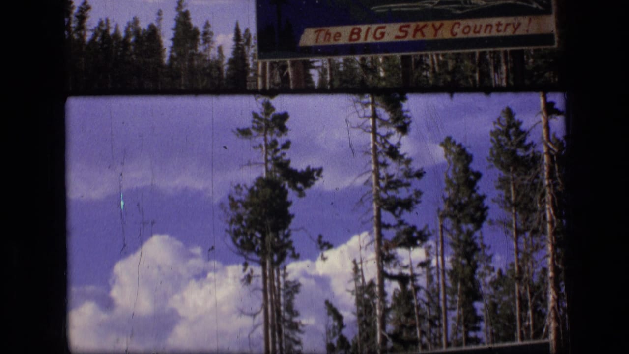 Evergreen trees and clouds beneath a partial Big Sky Country roadside sign.