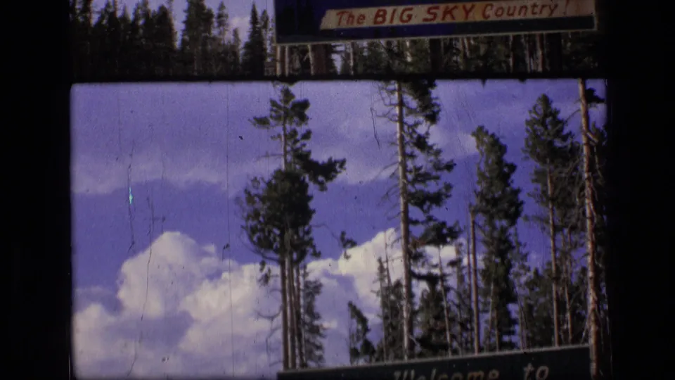 1973 Montana 8mm view of evergreen trees and bright clouds, with the Big Sky Country sign cropped along the upper frame.