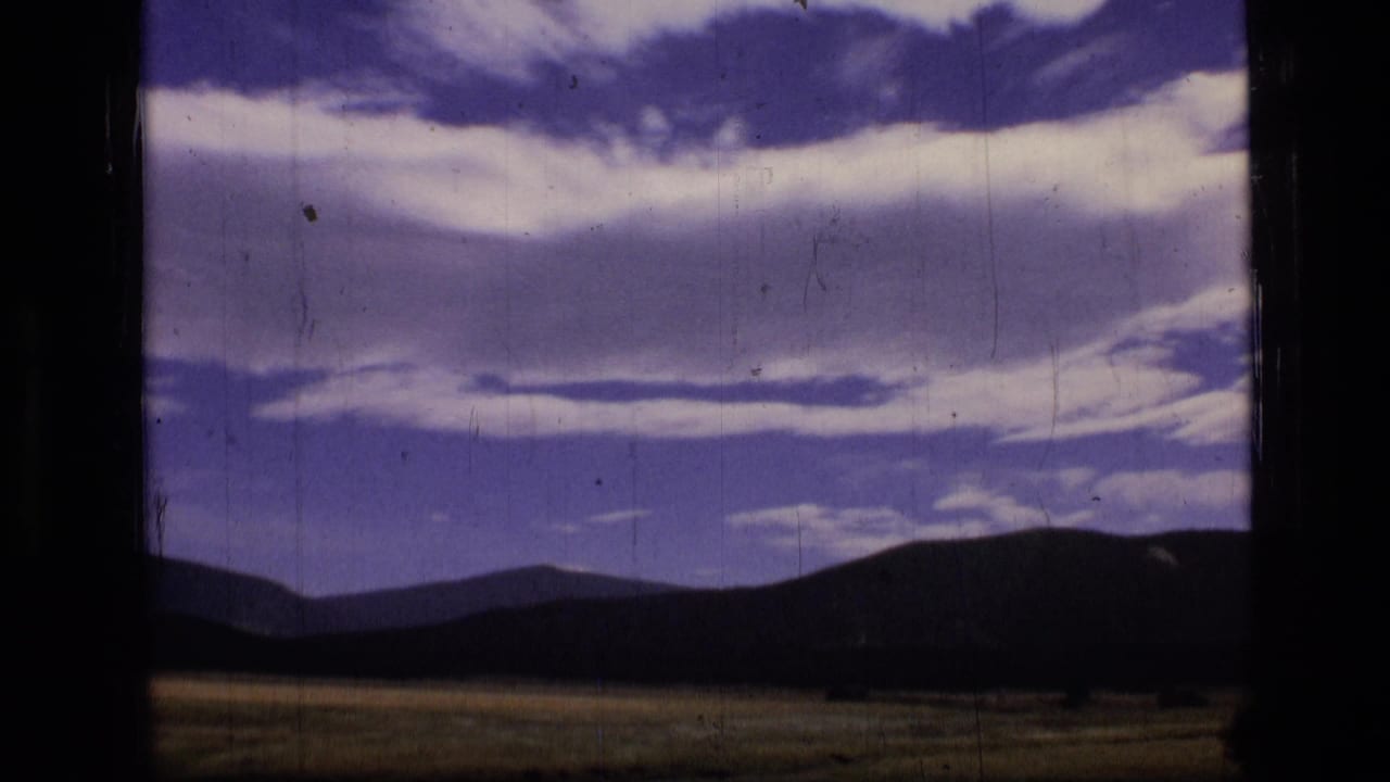 1973 Montana wilderness view with open grassland, silhouetted hills, and a cloud-heavy sky on faded 8mm or Super 8 film.