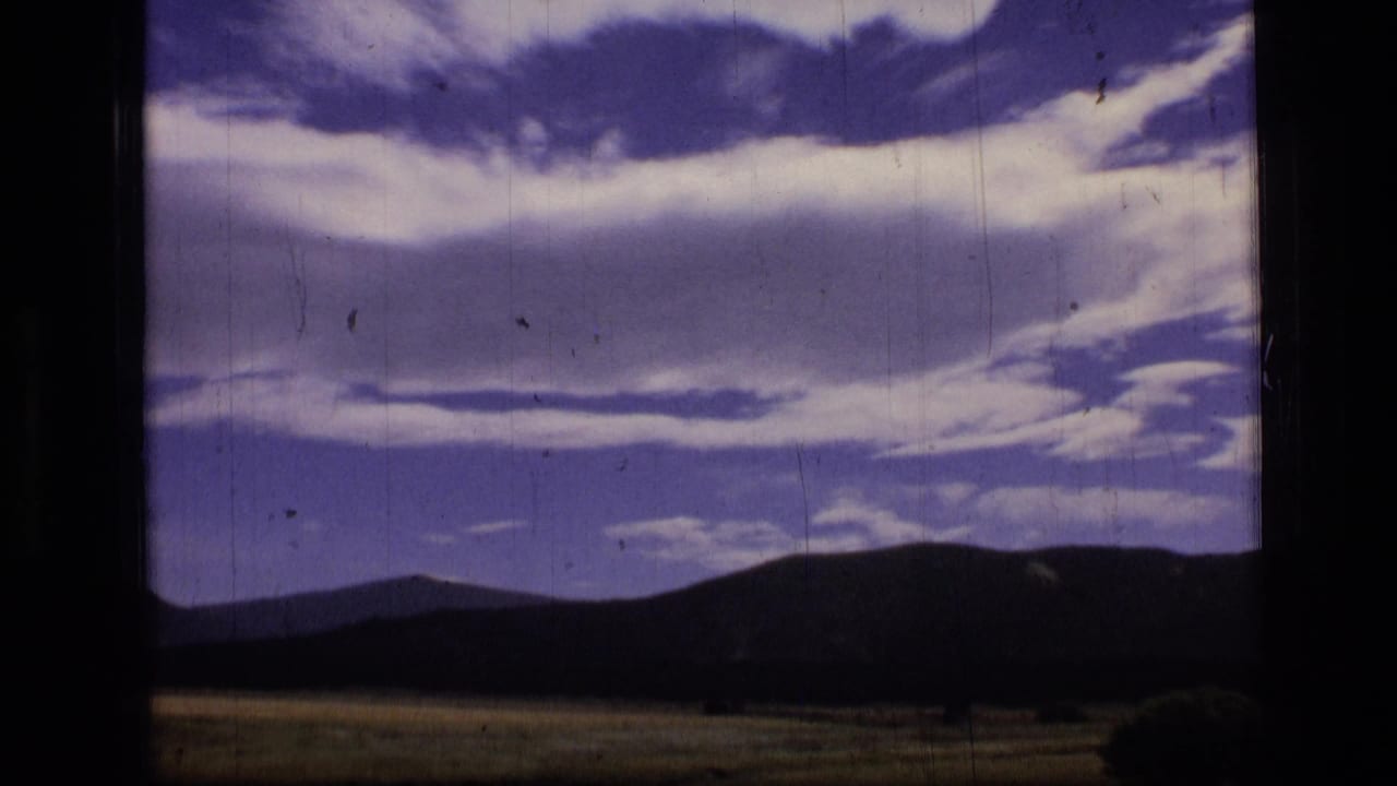 Wide Scapegoat Wilderness landscape with dark mountain silhouettes, grassy foreground, and faded color from 1970s home-movie film.