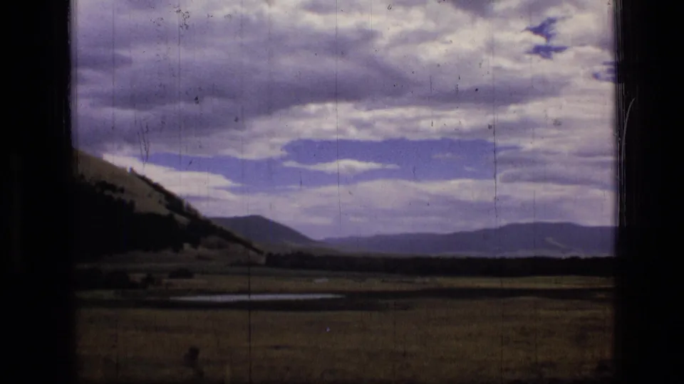1973 8mm view of Scapegoat Wilderness terrain, showing meadow, hillside, wet patches, and distant mountain ridges.