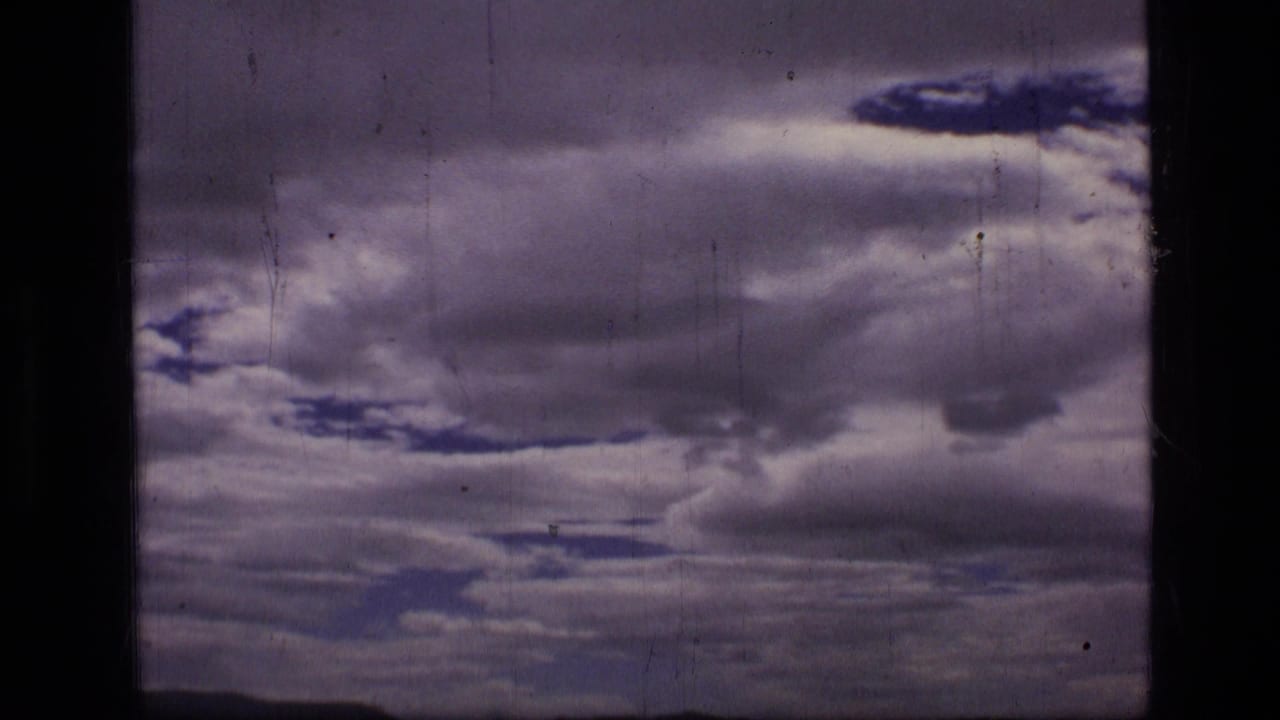 Dark purple-gray storm clouds fill the frame on scratched 8mm film.