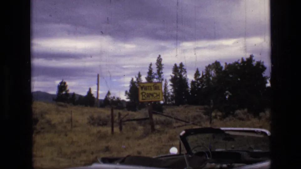 The roadside field view continues with the White Tail Ranch sign, fence line, trees, mountains, and convertible foreground in Montana.