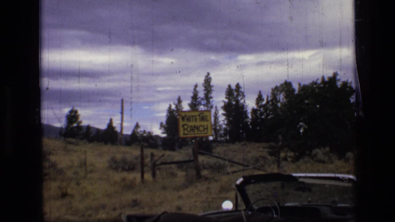 1973 8mm Montana travel frame showing a crooked yellow White Tail Ranch sign near a wooden fence, evergreens, cloudy sky, and partial car bodywork.