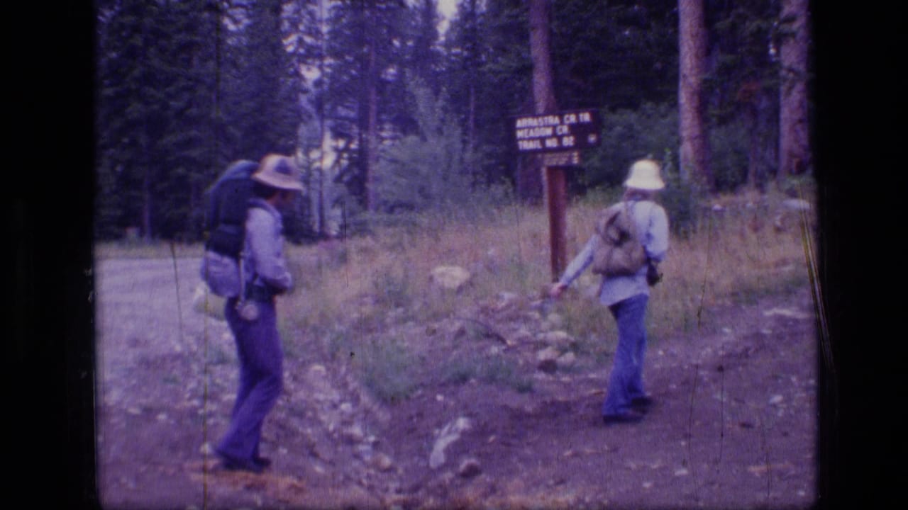 Two hikers with packs pause near a trail sign in Scapegoat Wilderness, Montana, in 1973 home-movie footage.