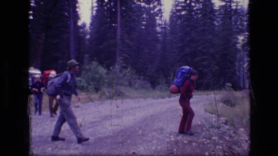 A small group of backpackers crosses a forest road or trail in 1973 Montana wilderness footage.