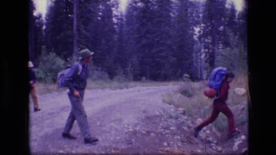 Backpackers pass across a forest trail in Scapegoat Wilderness, Montana, in 1973 8mm footage.
