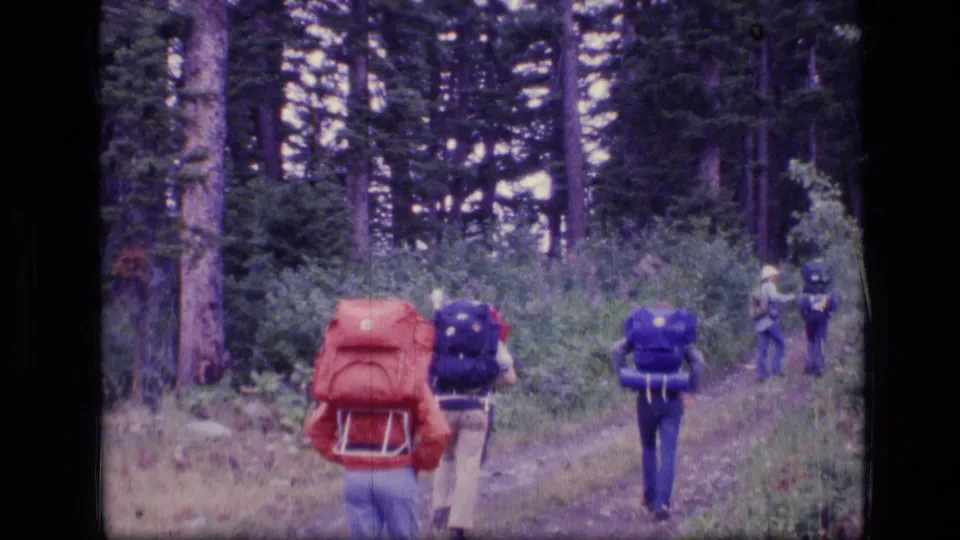 A rear-view 8mm frame shows backpackers walking deeper into the Scapegoat Wilderness forest in 1973.