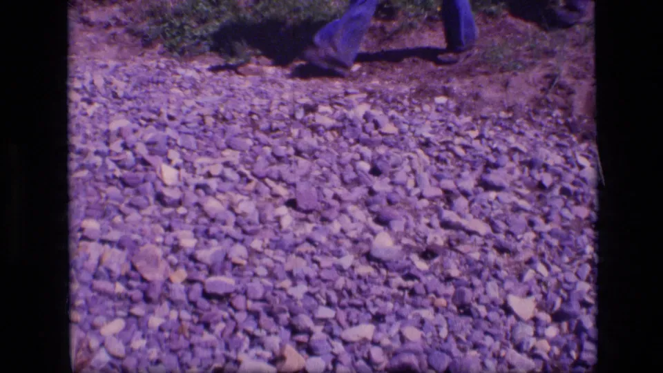 1973 Montana wilderness frame showing lower legs of a hiker walking across a rocky trail.