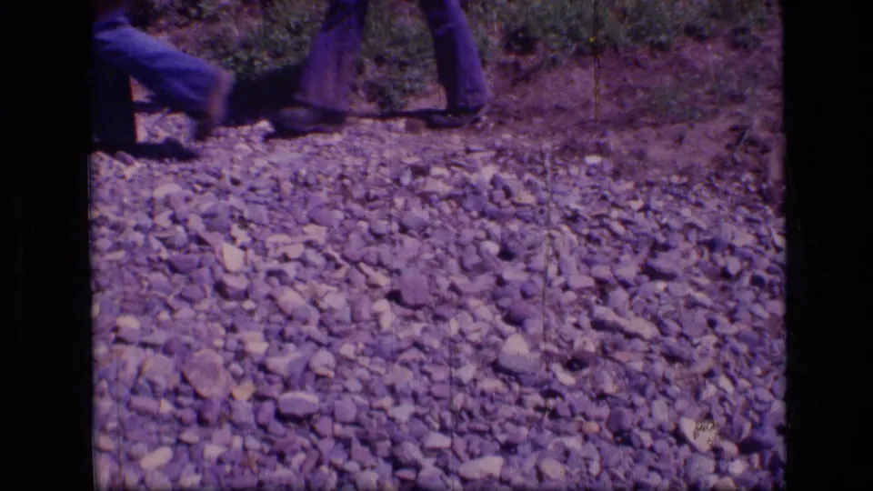 8mm frame from Scapegoat Wilderness showing hikers' lower legs crossing a gravel trail.