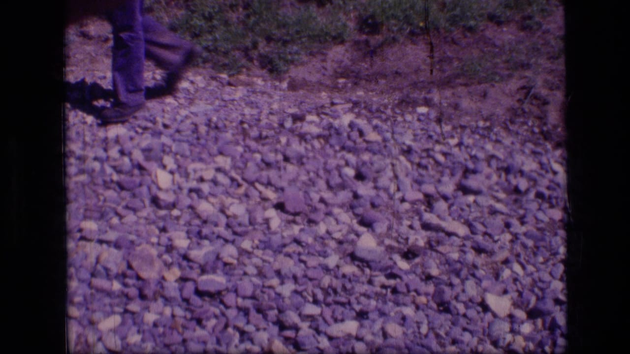 1973 8mm Scapegoat Wilderness frame showing a man's lower legs on a stony path with purple-blue film cast.