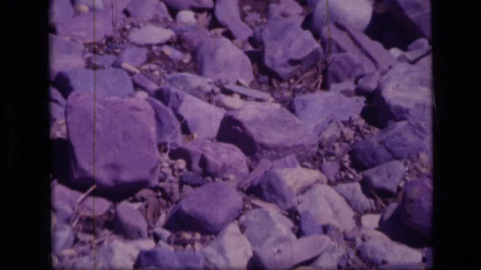 A 1973 home-movie view of rough Montana wilderness trail stones, framed close to the ground.