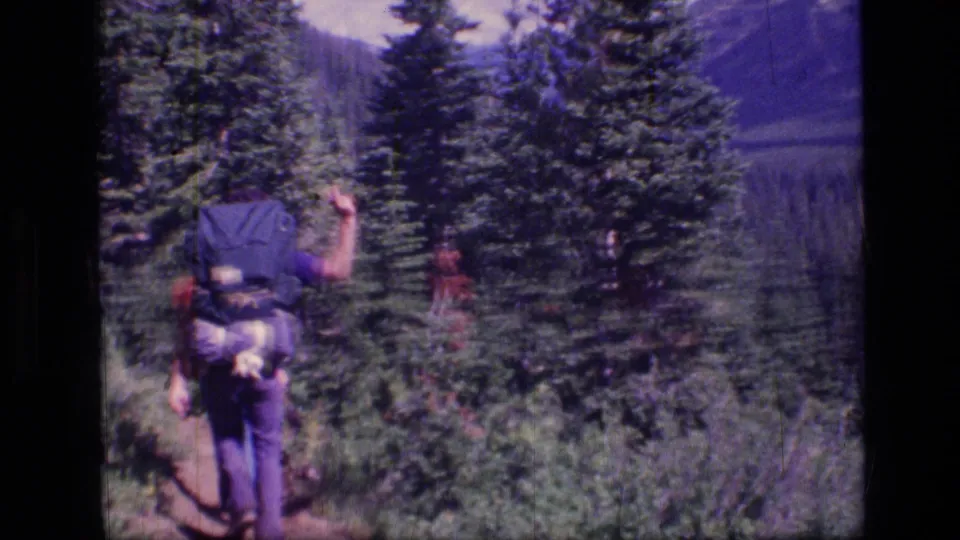 A backpacked hiker walks along a forest trail in the Scapegoat Wilderness, Montana, in 1973 8mm home-movie footage.