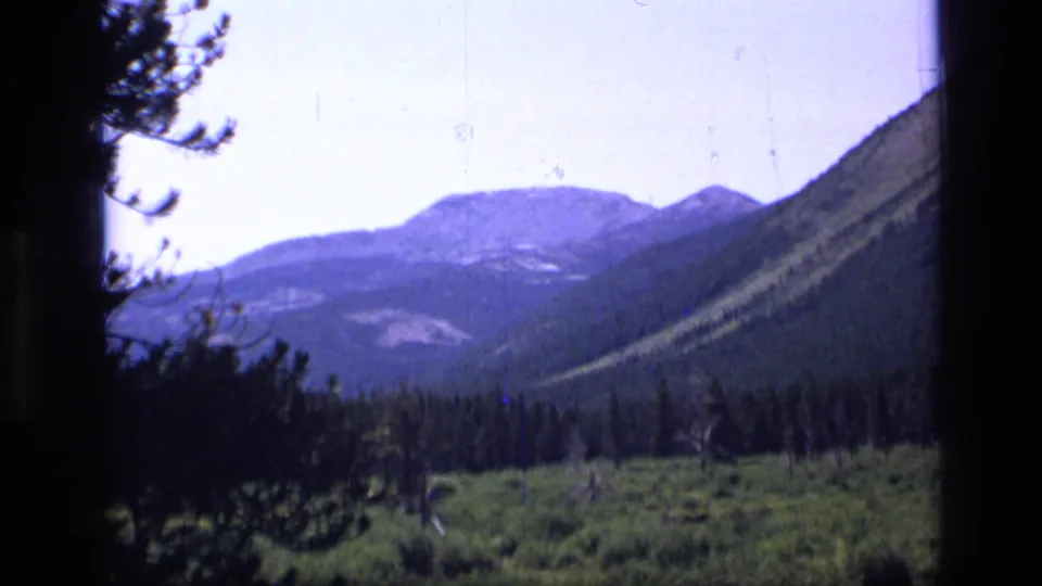 Scapegoat Wilderness mountain valley in Montana, filmed through dark foreground edges with pine forest and distant ridges.