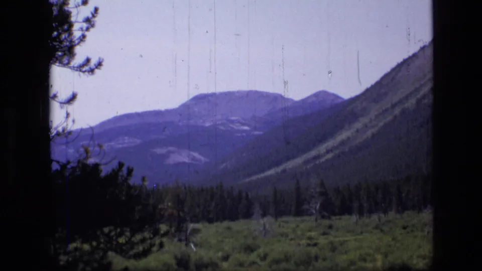 1973 8mm view of Montana mountain slopes and a green valley, with dark home-movie edge framing and visible film wear.