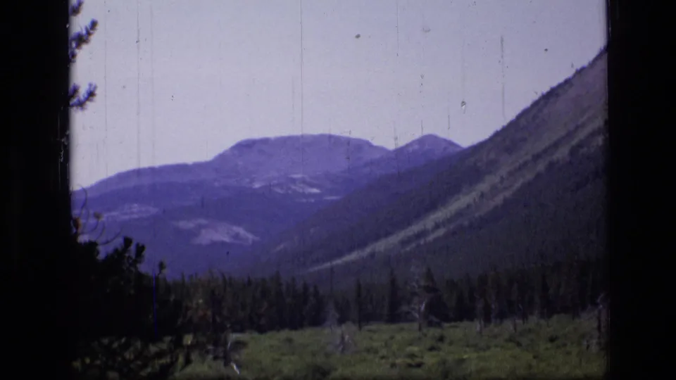 Scapegoat Wilderness landscape with distant ridges, forested valley vegetation, dark frame edges, and visible 8mm scratches.