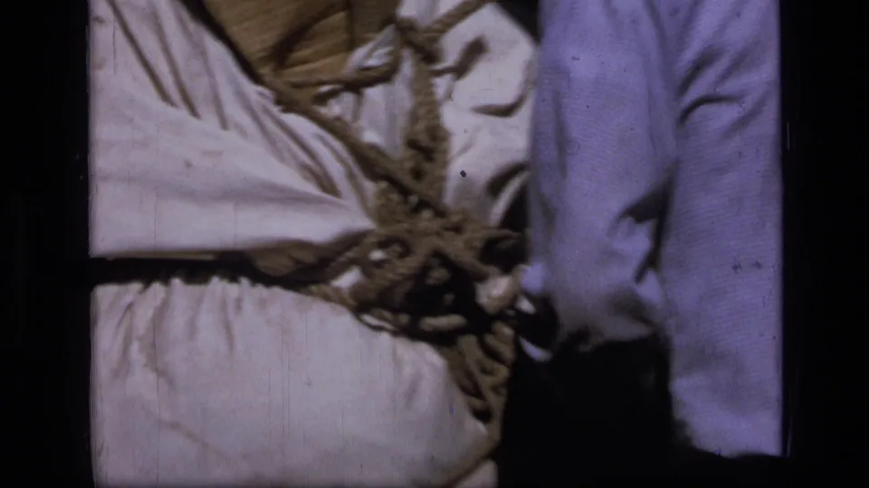 A rope knot and white canvas pack fill the frame as someone stands nearby during 1973 wilderness packing.