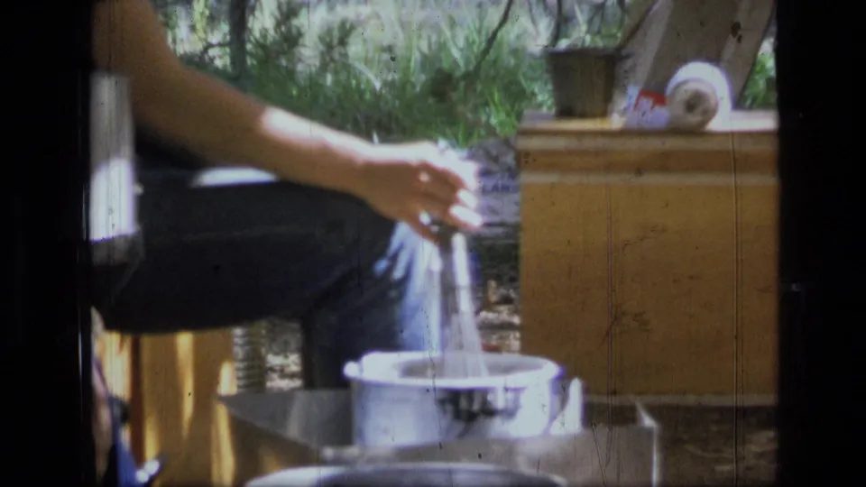 Close 8mm frame of camp cooking in Scapegoat Wilderness, with liquid poured near metal pots and a wooden chest.