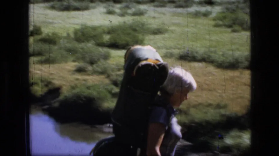 A closer, softer 8mm frame shows one backpacker moving through the Montana meadow near the stream.