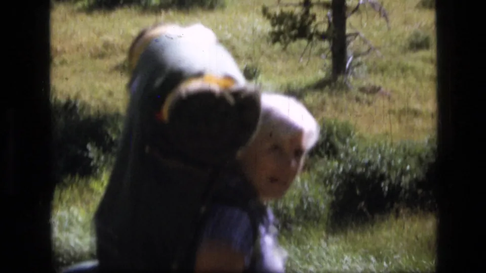 Close 8mm view of an adult backpacker in Scapegoat Wilderness, with meadow vegetation and trees behind.