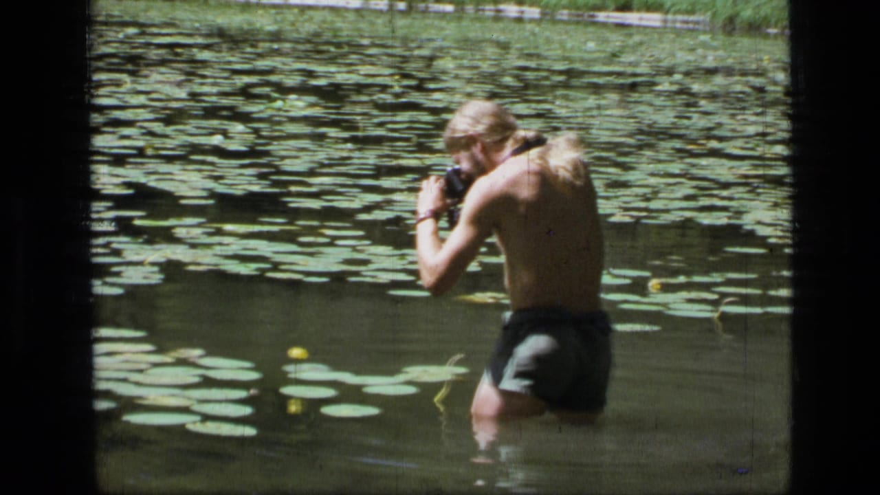 The man turns toward the water lilies in the Montana wilderness pond and brings his camera up to photograph them.