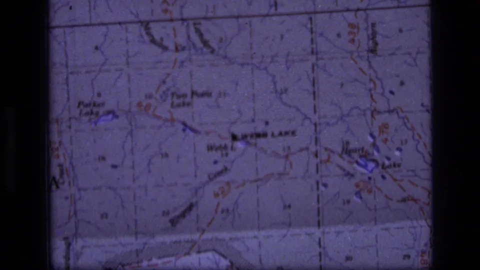 1973 8mm frame of a Montana wilderness topographic map, with lake labels, route markings, and soft purple film coloration.