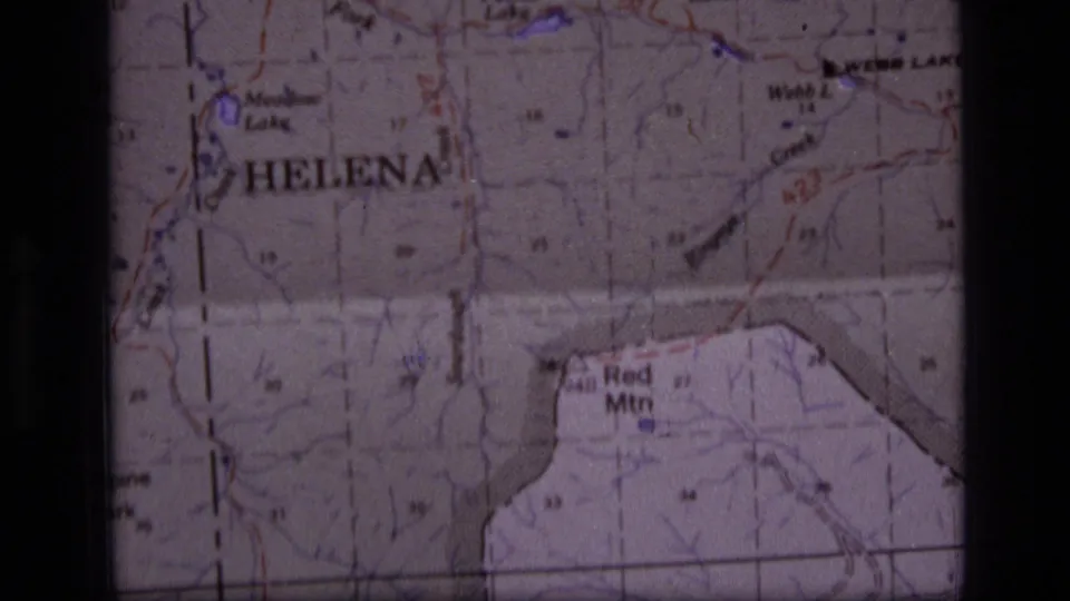 Soft 1970s 8mm frame of a Montana topographic map, with Helena and Red Mtn visible through grain, fold marks, and projection darkness.