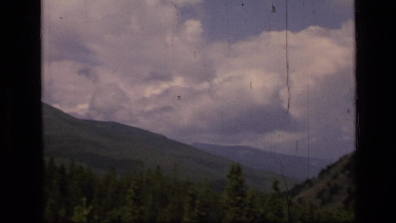 Forested mountain slope beneath a cloudy sky with dark film borders and scratches.